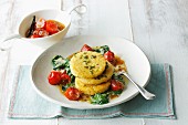 Millet cakes on a bed of tomatoes, spinach and orange sauce