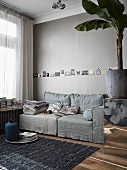 Wohnzimmer in warmen Grautönen mit einer Reihe angepinnter Postkarten über dem gemütlichen Sofa