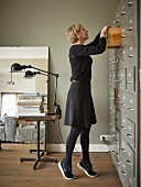 Young woman rummaging in drawer of old filing cabinet in front of table with industrial-style, vintage clip lamps