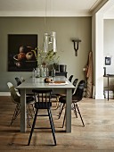 Essplatz mit Eames Stühlen und Kinderhocker an grau lackiertem Tisch mit Glasschirm-Leuchte; Stillleben an der Wand im Hintergrund
