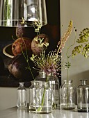 Single flowers in old glass bottles on dining table below pendant lamp with glass lampshade