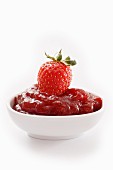 A bowl of strawberry jam topped with a fresh strawberry