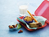 A lunchbox with a muffin, carrots, bread, dried fruits and milk