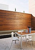 Dining area with white shell chairs in purist courtyard with wood-clad screen and floor-level pool