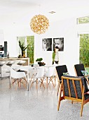 Open-plan interior in Australian beach house with 60s retro armchairs, classic shell chairs in dining area and concrete breakfast bar; black and white portraits of children