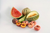 Various different melons and peaches against a white background
