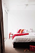 Schlafzimmer - weiße Bettwäsche und rote Kissen auf Doppelbett in minimalistischem Ambiente