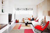 Designer living room with red, upholstered rocking chair next to woman sitting on couch and dog below window