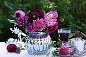 Pink dahlias in spherical, silver vase next to glass of red wine on silver tray in garden