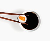 Maki sushi held in chopsticks over bowl of soy sauce