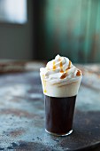 Coffee with whipped cream and caramel sauce on a metal surface