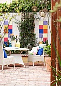 White, rattan outdoor furniture on terrace with terracotta floor and colourful tiles on courtyard wall