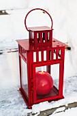 Red, spherical candles in red lantern on snowy wooden steps