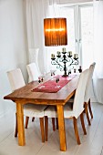 Dining table set with wine glasses and wrought iron candelabra, retro lamp with fabric lampshade and wooden chairs with loose covers