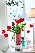 Red and white striped jug of red tulips on side table next to window