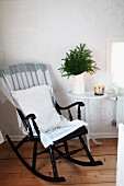 Black-painted wooden rocking chair with white cushion next to water jug of fir branches on side table