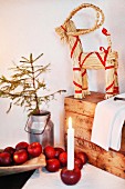 Weihnachtlich dekorierte Zimmerecke, rote Äpfel und in Apfel gesteckte Kerze vor Holztruhe, darauf Strohtier mit rotem Schleifenband verziert