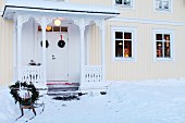 Verschneiter Vorgarten mit weihnachtlich dekoriertem Schlitten, vor hellgelbem Schwedenhaus mit überdachtem Hauseingang