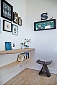 Dark wood Butterfly Stool by Sori Yanagi in corner next to books and ornaments on wooden, wall-mounted shelves below framed pictures