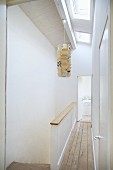 Schmaler Gang mit Holzdielenboden neben Treppenaufgang, darüber Hängeleuchte aus Papier an Decke mit Oberlicht Fenstern