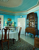 Grand dining room painted light blue with set table opposite display cabinet
