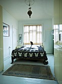 Blick ins Schlafzimmer einer Altbauwohnung mit minimalistischem Flair, französisches Bett und folkloristische Tagesdecke vor Fenster mit Lamellen Jalousie