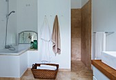 Laundry basket on floor between fitted bathtub in niche and shower area with beige, marbled tiles on walls and floor