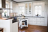 weiße Einbauküche mit umlaufendem Fries und Einbauleuchten, freistehender Küchenwagen