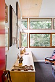 Pale wooden sideboard against wall and ribbon windows with view of trees