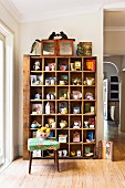 Flea-market finds on old wooden shelves against wall, fruit bowl on retro stool on wooden floor in traditional interior