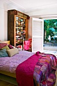 Patchwork bedspread on double bed, antique bookcase and open terrace doors with view of palm trees