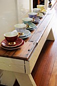 Espresso cups of various colours with gilt handles lined up on rustic wooden bench