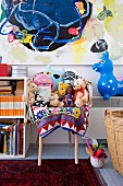 Soft toys on armchair and animal hopper below colourful painting in child's bedroom