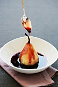 Red wine sauce being poured over a poached pear