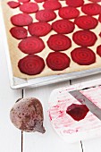 Slices of beetroot on a baking tray with a knife and a beetroot next to it