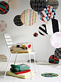 Various large colourful fabric circles of various patterns hanging in interior, stacked blankets on white metal chair and white wooden floor