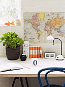 Money tree in dark pot and office utensils next to white desk lamp on table below map of world hung on whitewashed brick wall