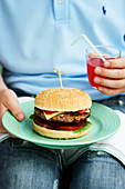 A child holding a cheeseburger on a plate