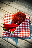A bowl of red chilli peppers and chilli threads on a tea towel on a wooden table