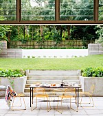 Breakfast table in seating area on terrace of architect-designed house with modern garden pool in background