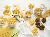 Various sorts of pasta, some in jars and some on a wooden surface