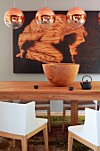 Spherical, copper pendant lamps above wooden bowl on table and chairs with white backrests and arms