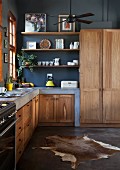 Masonry kitchen counters with solid wooden doors in open-plan kitchen with black-painted wall and animal-skin rug on polished concrete floor