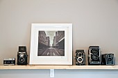 Black and white cityscape flanked by collection of old cameras on wall-mounted shelf