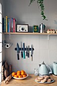 Still-life arrangement in corner of kitchen with cookery books, radio and kitchen utensils on shelf above magnetic knife rack