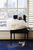 Bouquet of white flowers wrapped in paper on black upholstered chair and sling-back high heels on carpet below lattice window