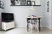 Dining area with vintage chairs and metal locker on castors used as TV cabinet below gallery of black and white pictures