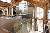 Designer, stainless steel, fitted kitchen in modern chalet with exposed wooden roof structure and glass walls
