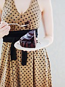 A woman in a spotted dress eating a slice of chocolate cake