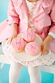 Mädchen in rosa Kleidung hält Teller mit rosa Cupcakes